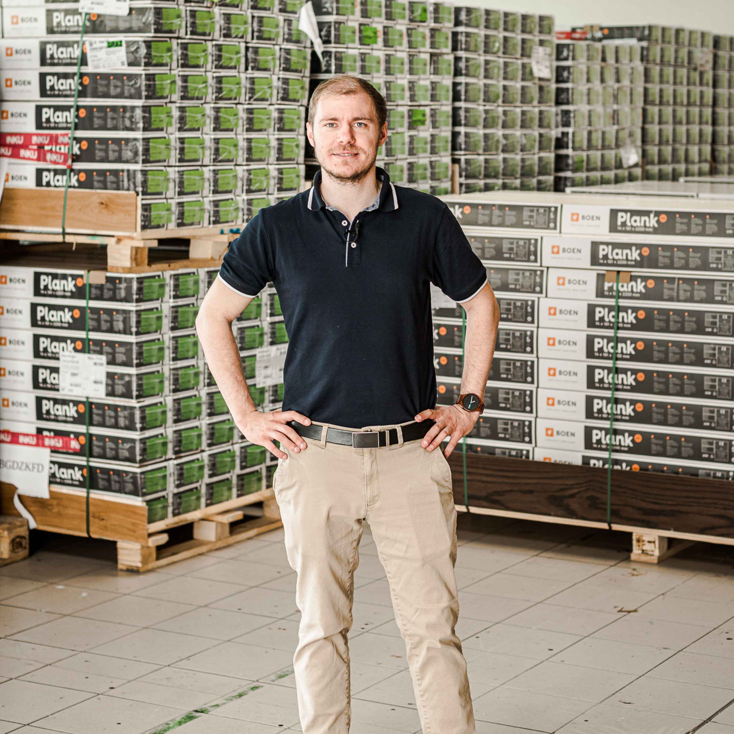 Bild zeigt Christian Wipfler stehend vor gestapelte Bodenbelägen in einer Lagerhalle.