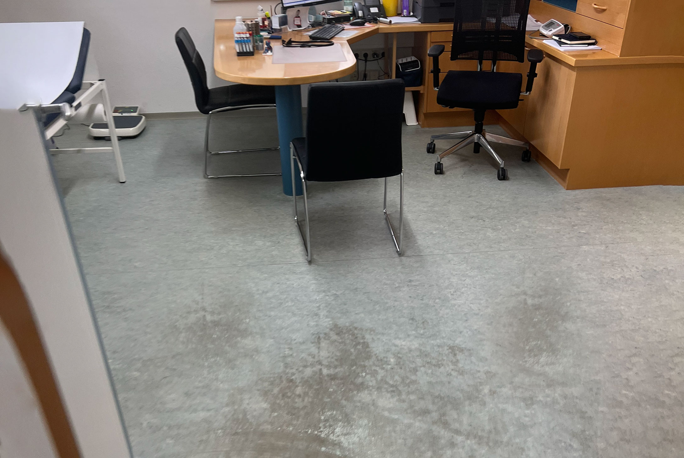 Bild zeigt beschädigten grauen Kunststoffboden vor der Sanierung einer Arztpraxis