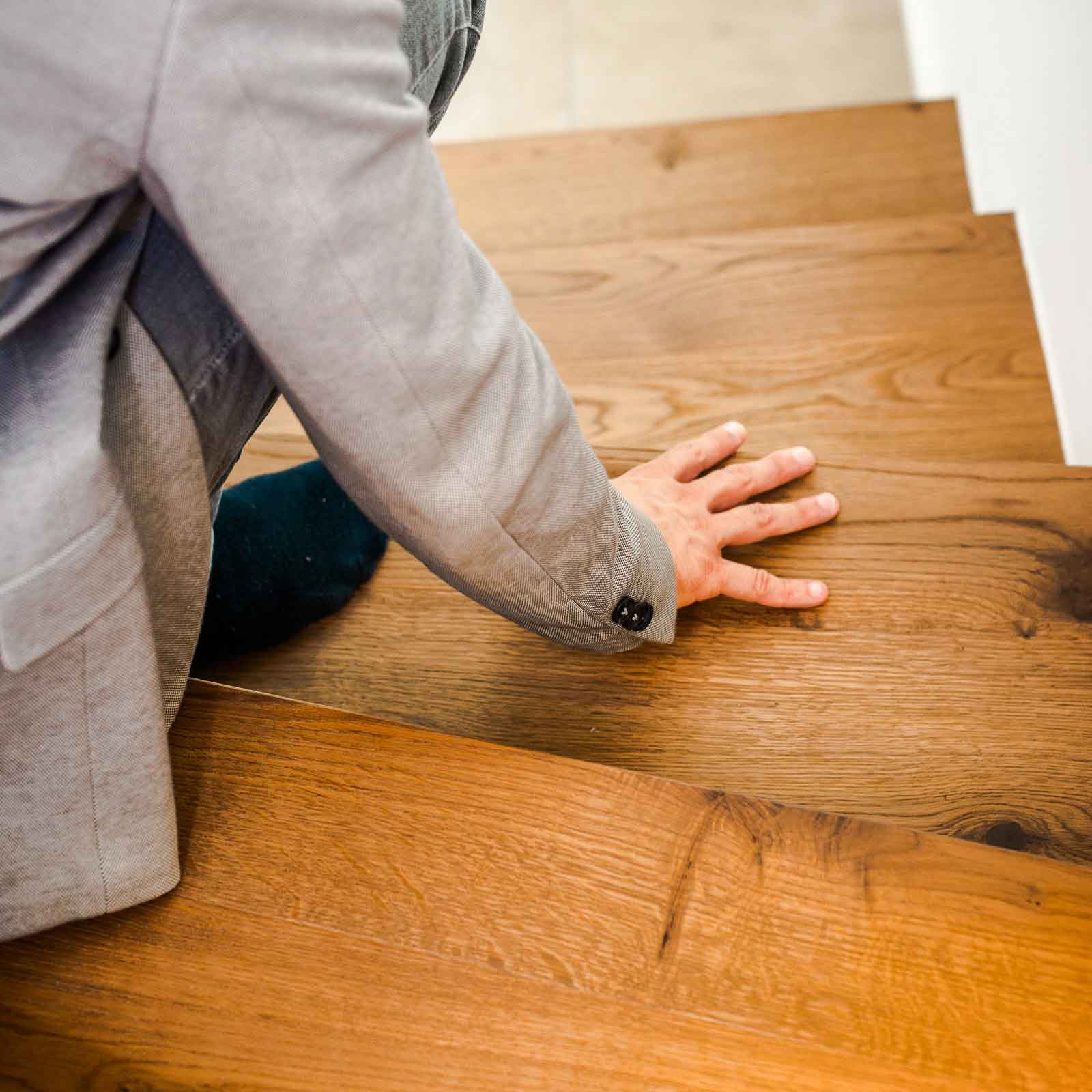 Bild zeigt Detailfoto von Christian auf Holztreppe sitzend und mit der Hand über den Boden streichend.