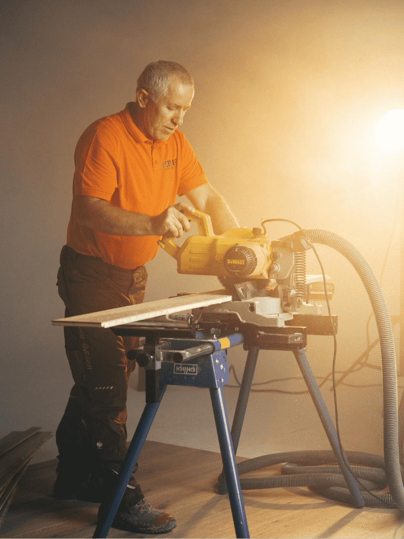 Bild zeigt einen Mitarbeiter beim Zuschneiden eines Holzboden in warmer Lichtatmosphäre.