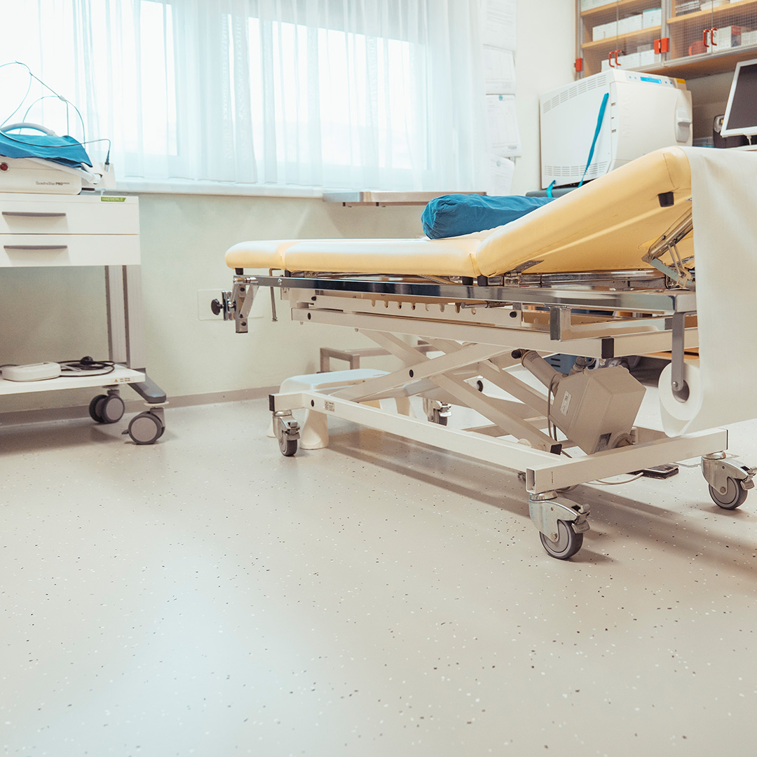 Bild zeigt sanierten hellen Kunststoffboden eines behandlungszimmers mit Liege und Gerätschaften.